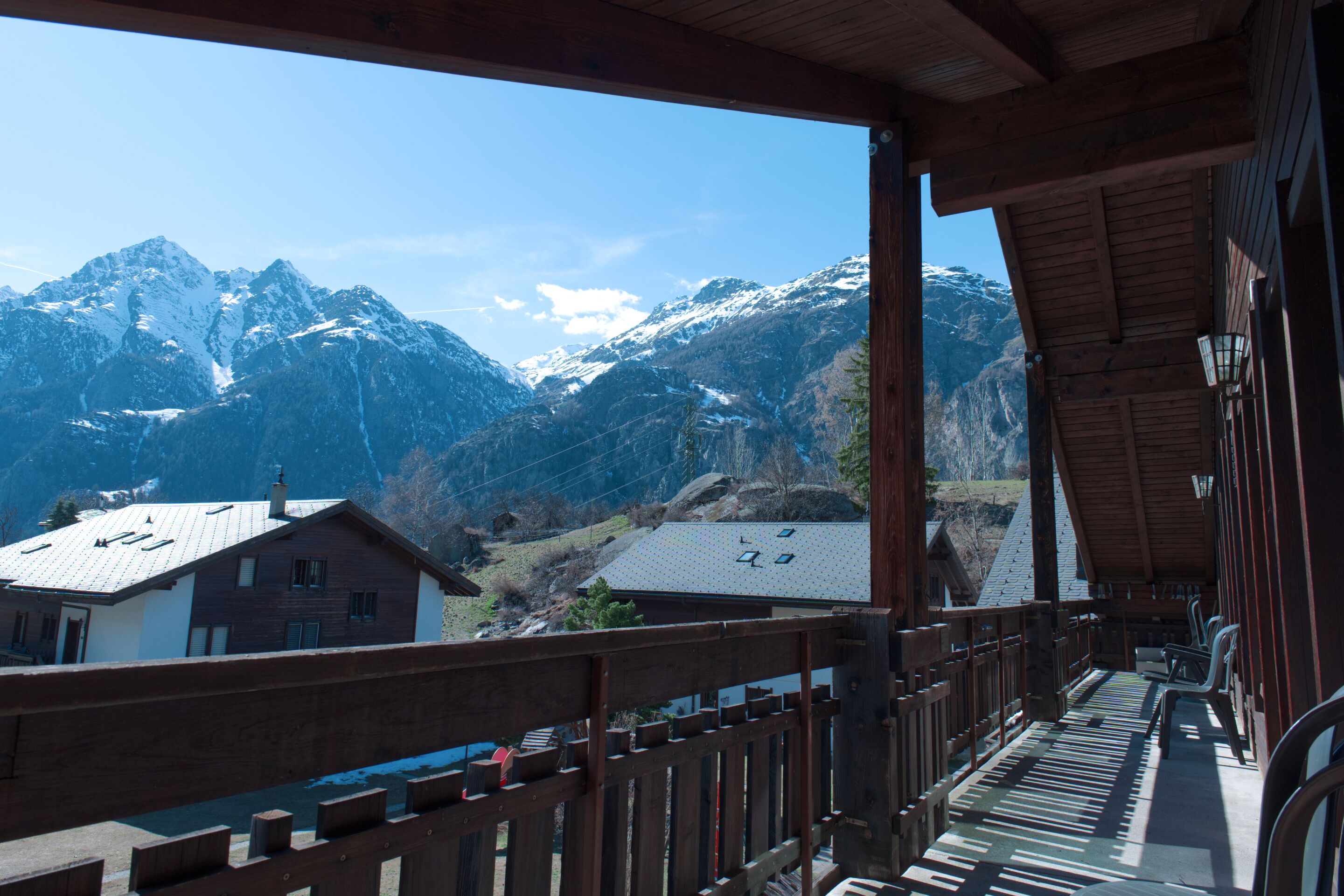 Un balcón de madera con vistas a montañas nevadas y un pequeño edificio de techo inclinado.