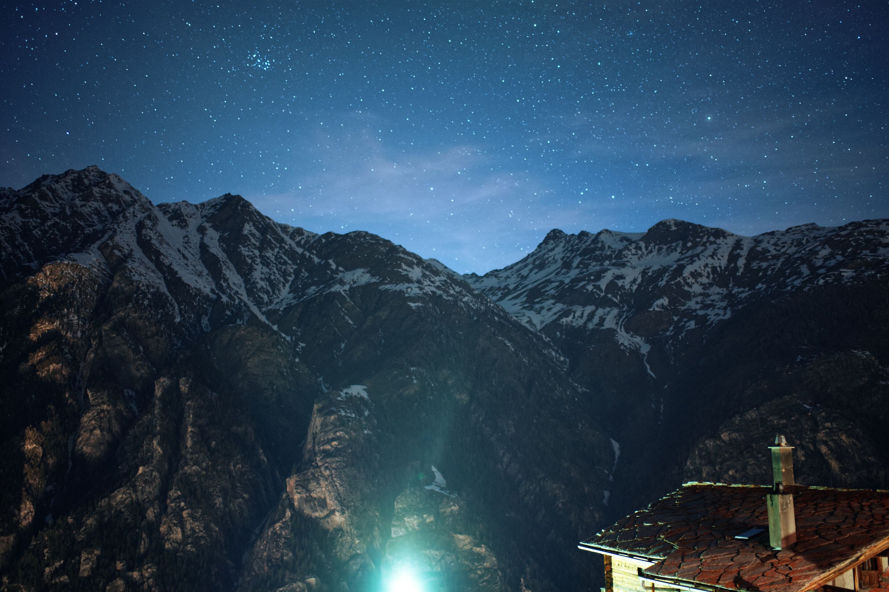 Uma cordilheira sob um céu estrelado, com uma casa em primeiro plano.