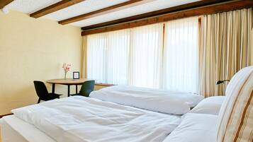 A hotel room with two beds, a small table, and a chair.