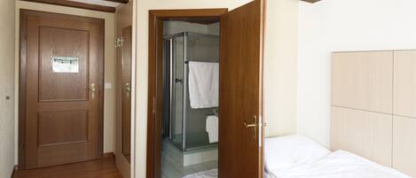 A bedroom with a wooden door, a glass shower, and a bed with white bedding.
