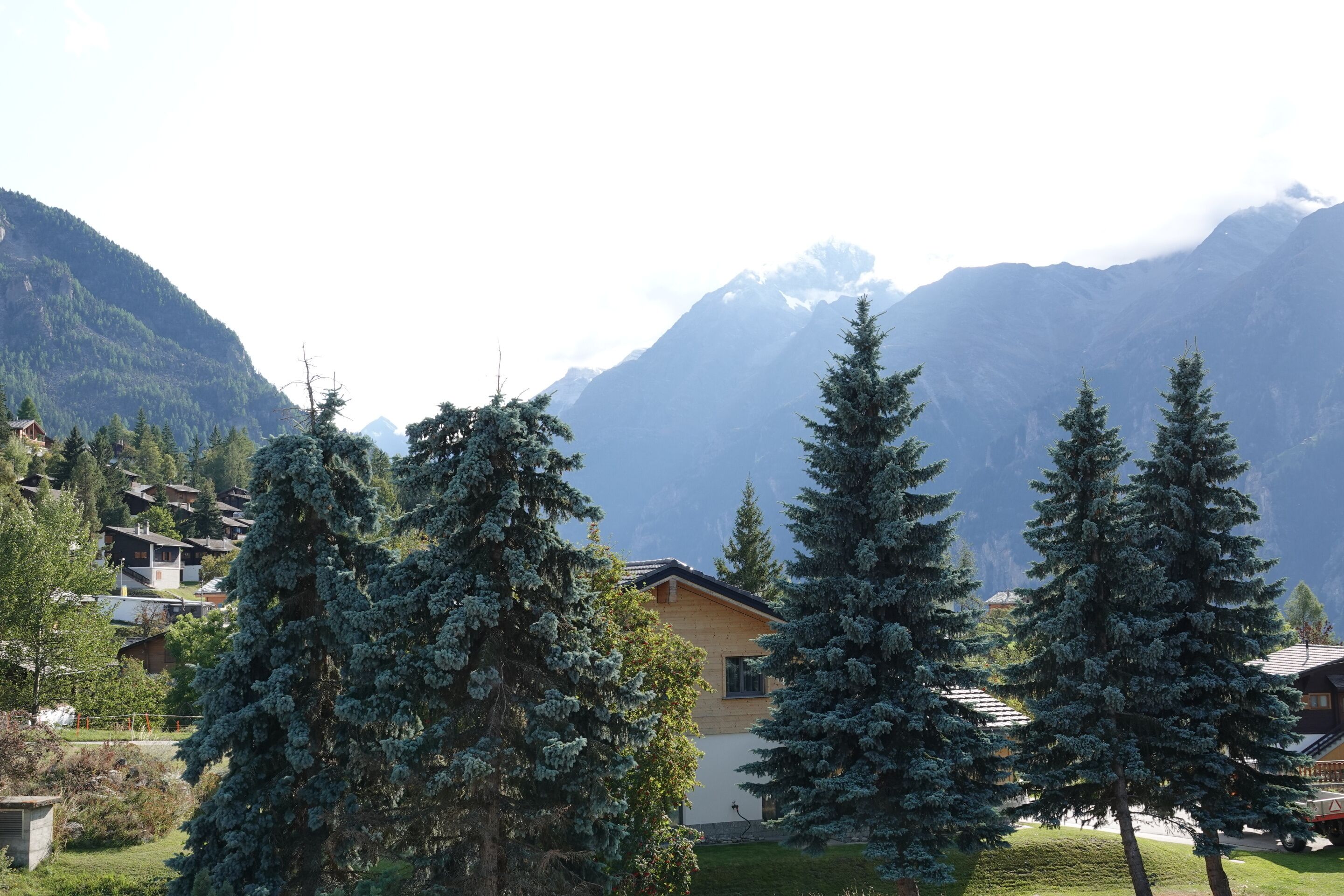 Un paysage de montagne avec des maisons, des arbres et un ciel dégagé.