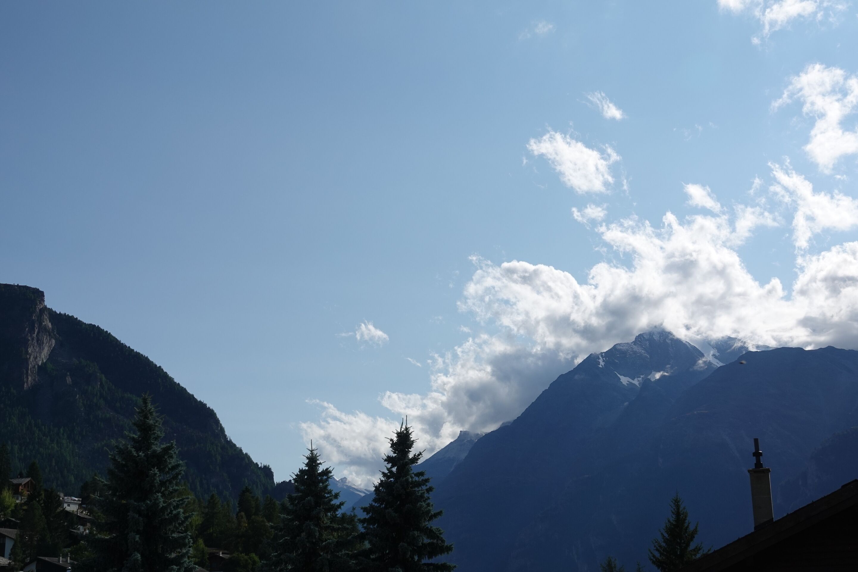 Eine Berglandschaft mit blauem Himmel, einem Kirchturm und immergrünen Bäumen.