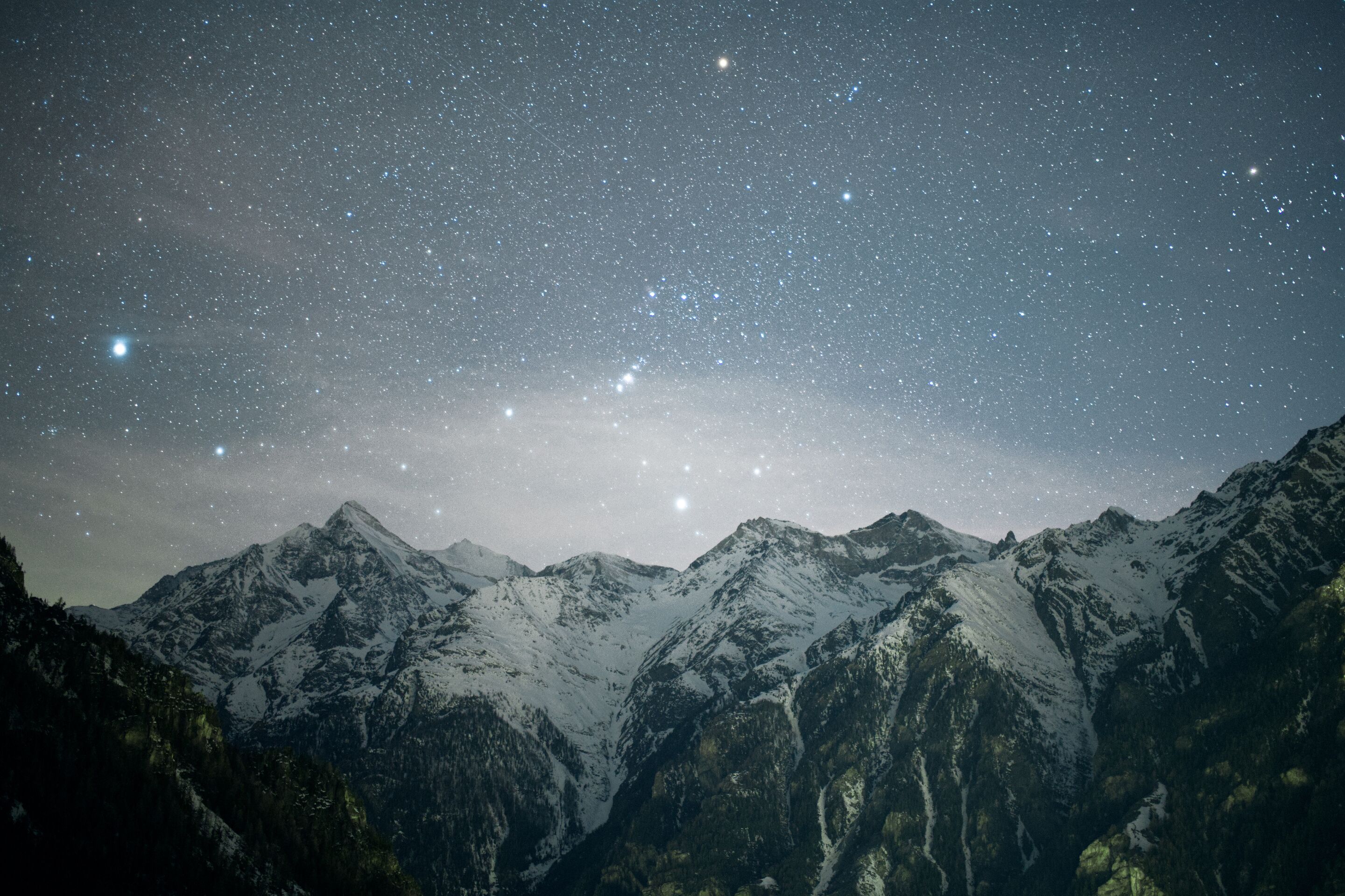 A starry night sky over snow-covered mountains.