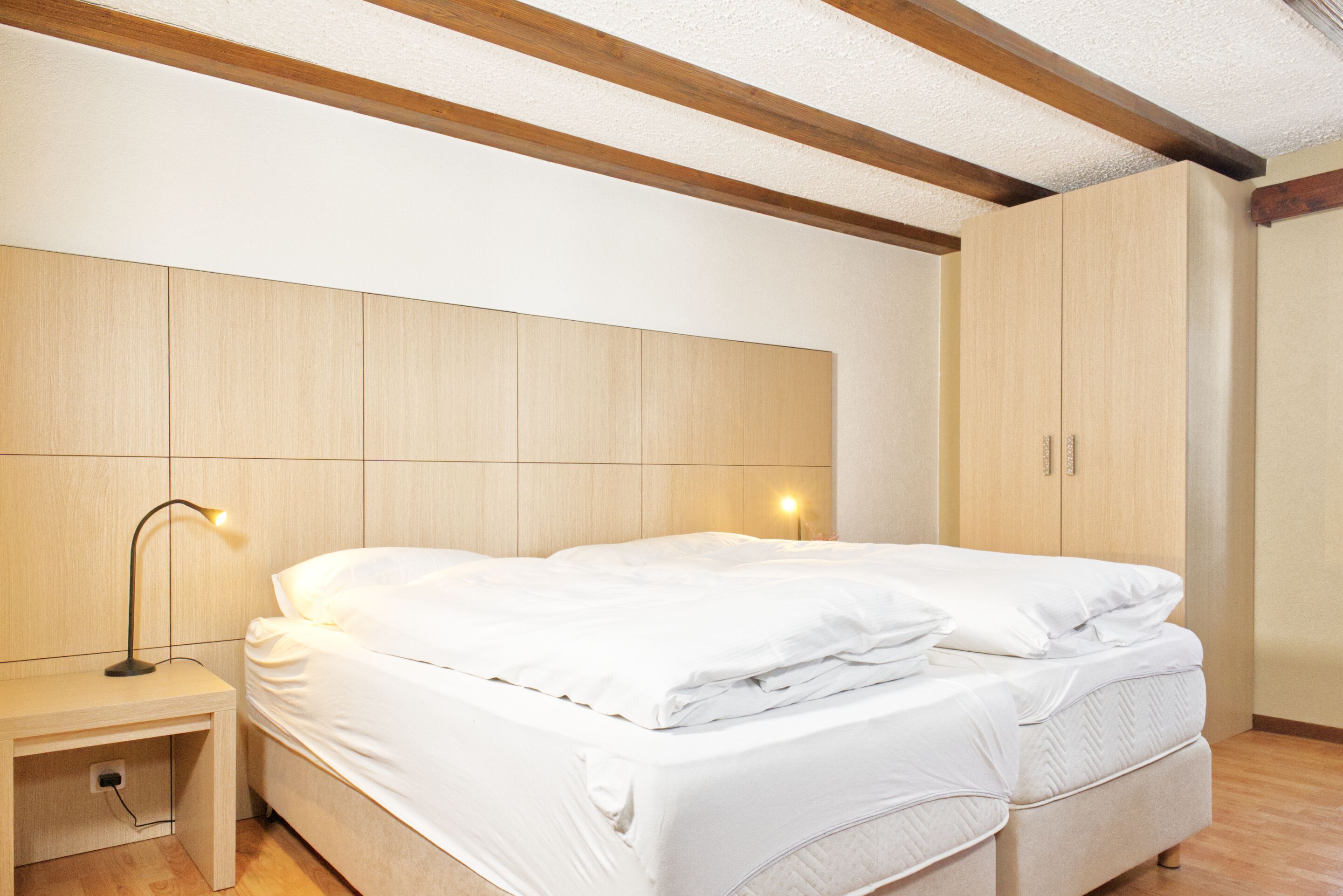 A bedroom with a bed, bedside table, lamp, and wooden wardrobe.