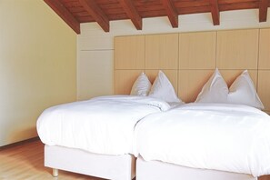 A double bed with white bedding in a room with wooden beams on the ceiling and a light-colored wall. - Alpia FlexiHomes (Graechen)