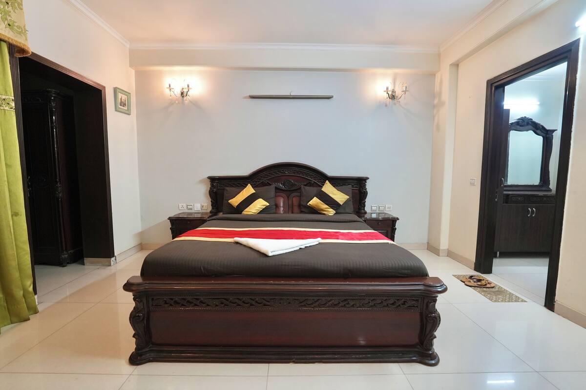 A bedroom with a large bed, a nightstand, a wall-mounted light, and a door.