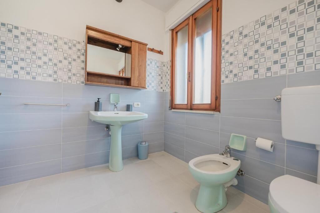 Et badeværelse med et håndvaskesæt, et bidet, et toilet og et vindue med trærammer.