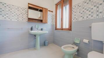Et badeværelse med et håndvaskesæt, et bidet, et toilet og et vindue med trærammer.