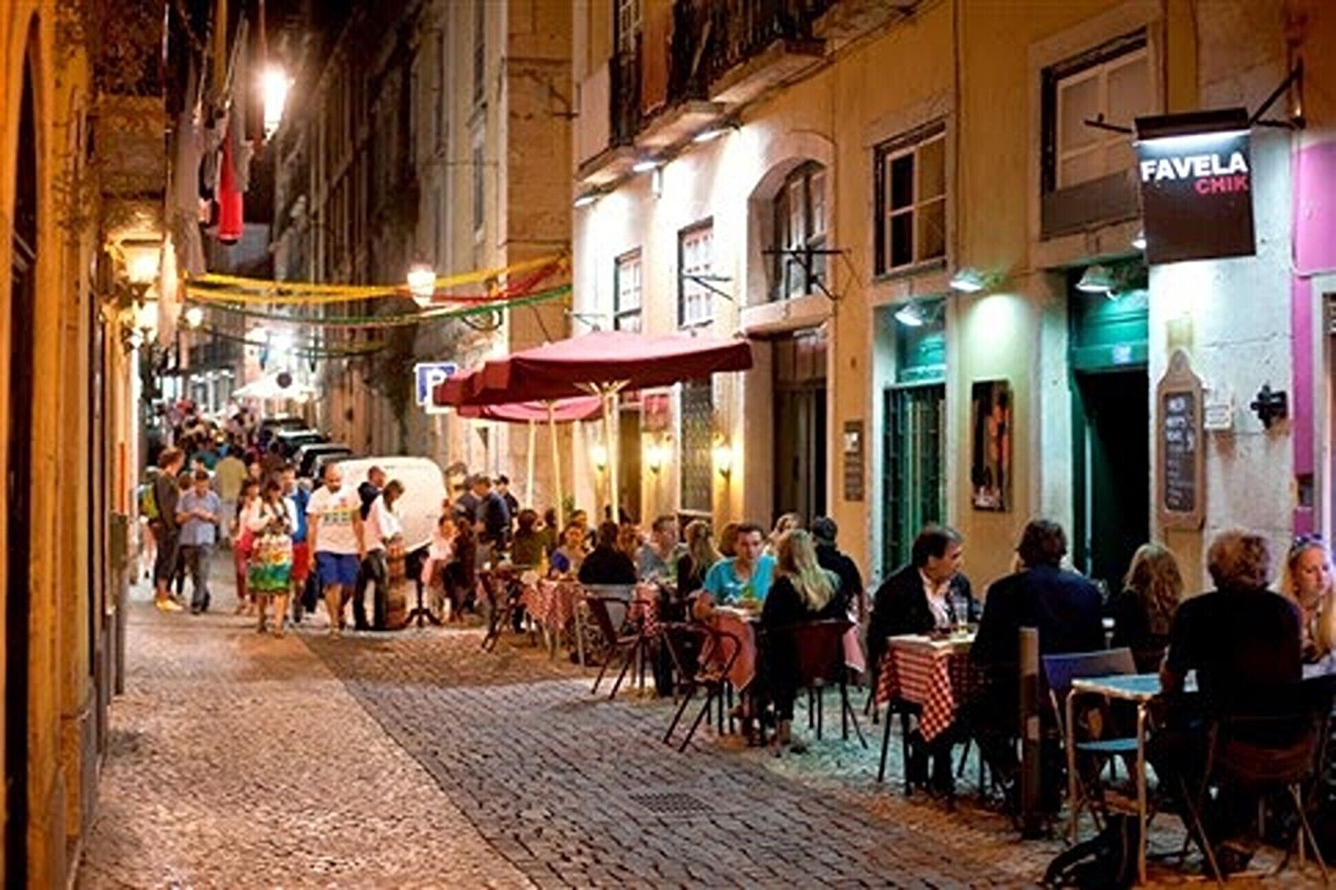 Une rue pavée bordée de terrasses de différents cafés, où l’on peut voir des gens manger et se promener.