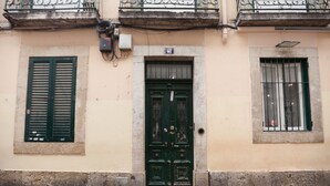 Eine Gebäudefassade mit einer grünen Tür, einem Fenster mit grünen Fensterläden und einem Balkon mit Eisengeländern.