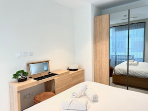 A modern hotel room with a bed, a desk with a computer, a small plant, and a view of the outdoors through a sliding door. - Cozy Mercury Tower w/RooftopPool by ArcoCollection (St. Julian`s)