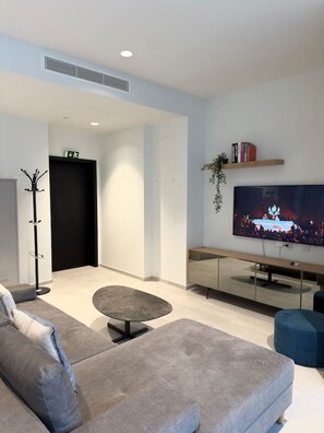 A modern living room with a flat-screen TV, a sofa, a coffee table, and a bookshelf. - Cozy Mercury Tower w/RooftopPool by ArcoCollection (St. Julian`s)