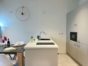 A modern kitchen with a central island, a built-in oven, and a wall-mounted clock. - Cozy Mercury Tower w/RooftopPool by ArcoCollection (St. Julian`s)