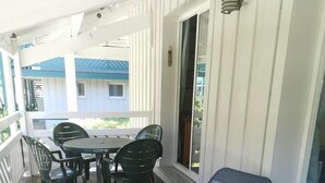 Varanda coberta com mesa e cadeiras, uma poltrona azul e vista para um edifício com telhado azul.