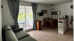 Sala de estar com sofá, mesa de jantar e área de cozinha, com placa indicando proximidade da praia.
