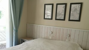 Quarto com uma cama, janela com cortinas e três quadros na parede.