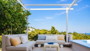 Ein Sitzbereich im Freien mit einer Couch und einem Tisch, einer Pergola und Meerblick.
