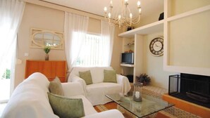 A living room with a sofa, a glass coffee table, a television, a fireplace, and a chandelier. - Porto Cheli 4Bedroom Villa Plunge Pool & SeaView 2 (Kosta)