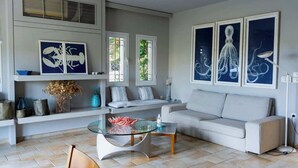 A modern living room with a glass coffee table, a sofa, and artwork on the walls. - Porto Cheli 4Bedroom Villa Plunge Pool & SeaView 1 (Kosta)