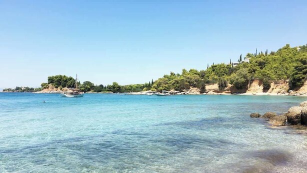 A beach with clear water, a boat, and a rocky shoreline with trees. - Porto Cheli 4Bedroom Villa Plunge Pool & SeaView 1 (Kosta)