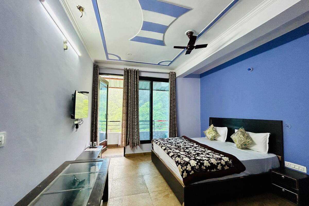 Un dormitorio con cama, televisor, ventilador de techo y vistas al exterior.