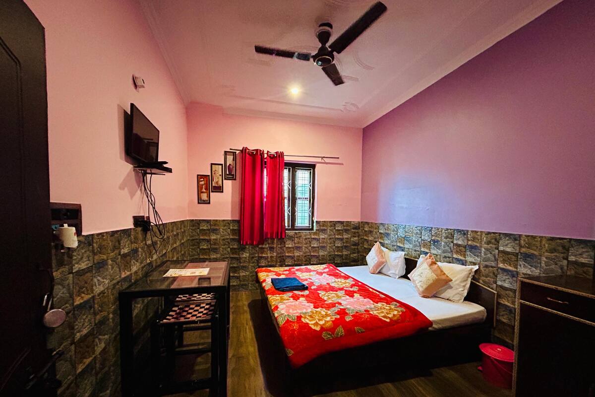 Un dormitorio con cama, escritorio, silla, ventilador de techo y televisor en la pared.