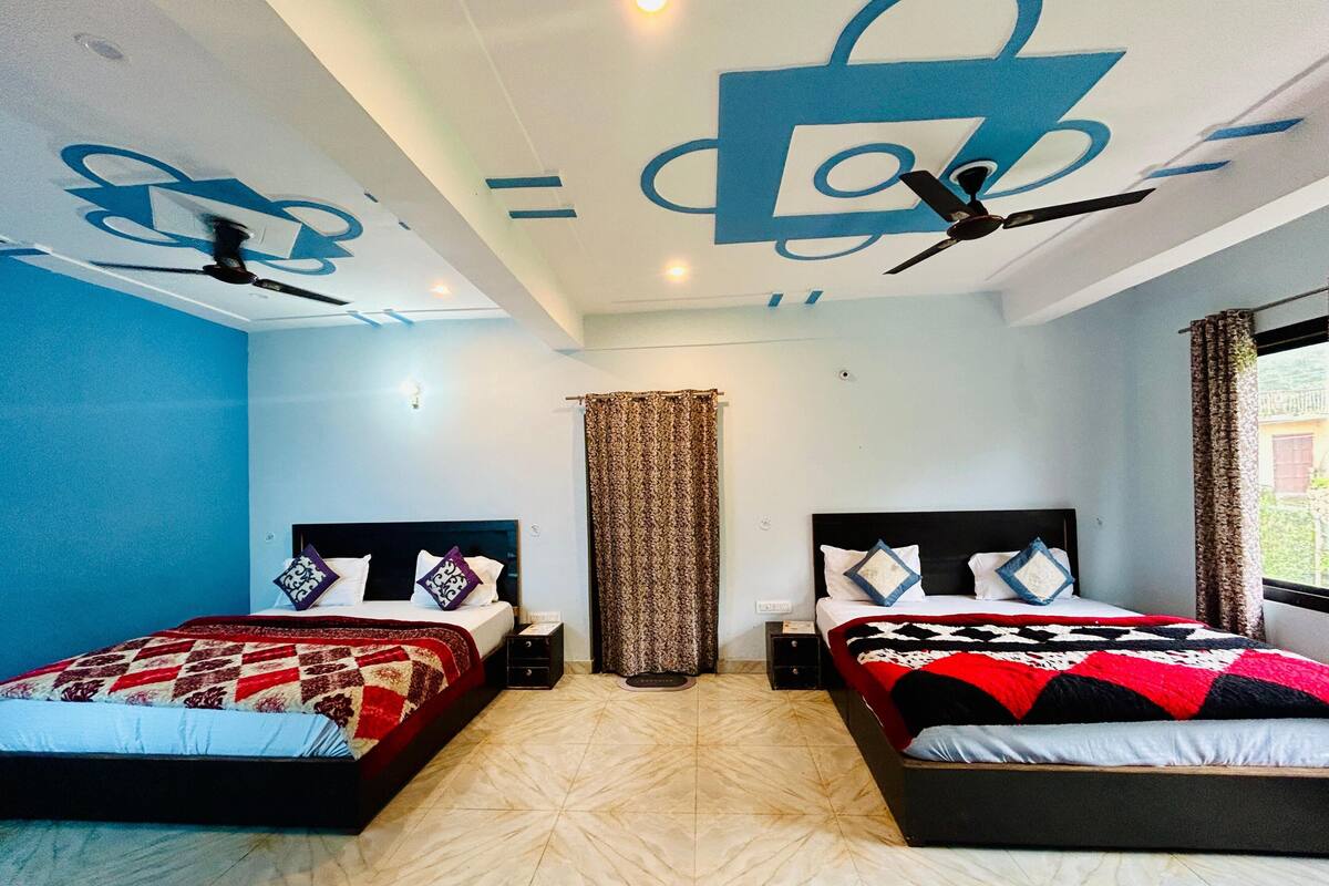 Habitación de hotel con dos camas, ventilador de techo, ventana grande con cortinas y piso estampado.