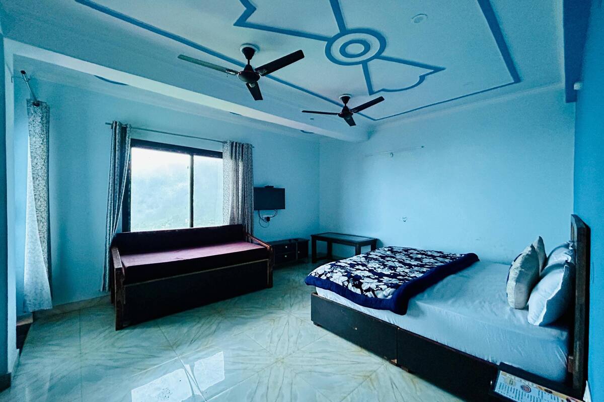 Un dormitorio con una cama, un banco, un ventilador de techo, un televisor y una ventana.