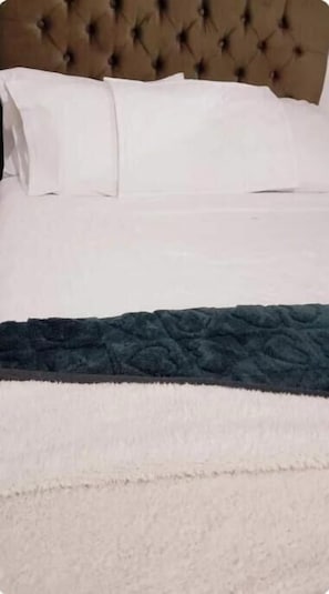 Een bed met een gestoffeerd hoofdbord, witte beddengoed en een donge deken.
