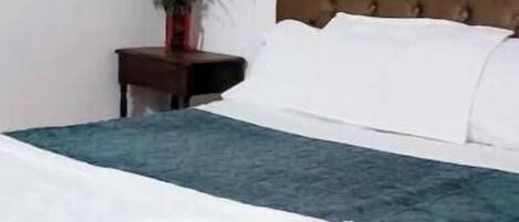 A neatly made bed with a brown headboard, a potted plant on a nightstand, and a framed picture on the wall.
