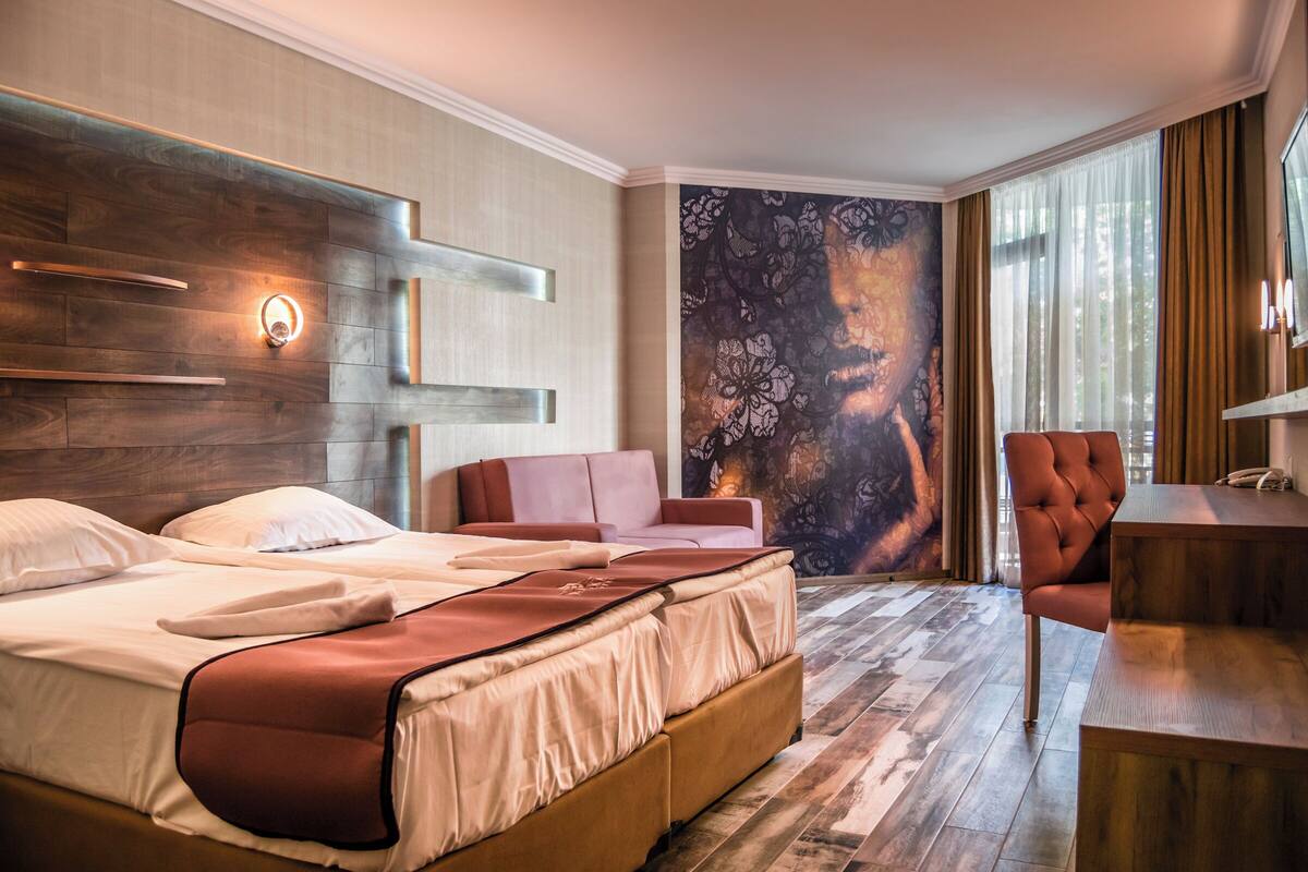 A hotel room with a large bed, a desk, a chair, and a wall mural.