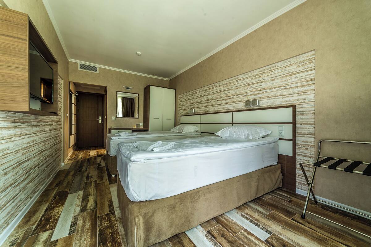 A hotel room with a large bed, a wardrobe, a mirror, and a wooden floor.