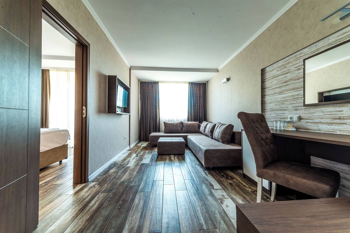 A modern living room with a sectional sofa, a flat-screen TV, and a wooden floor.