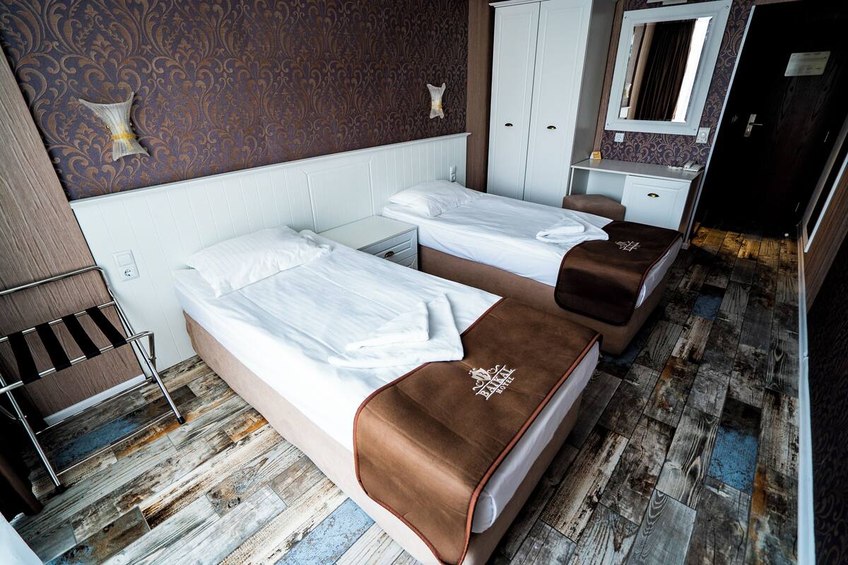 A hotel room with two beds, a wardrobe, a mirror, and a wooden floor.