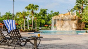 Un área de piscina con sillones de descanso, una pequeña mesa con una bebida y una cascada.