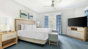 Habitación de hotel con cama, escritorio, silla, televisión y ventilador de techo.