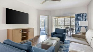 Uma sala moderna com televisão de tela plana, um armário de madeira, uma poltrona azul, um sofá e uma varanda com vista.