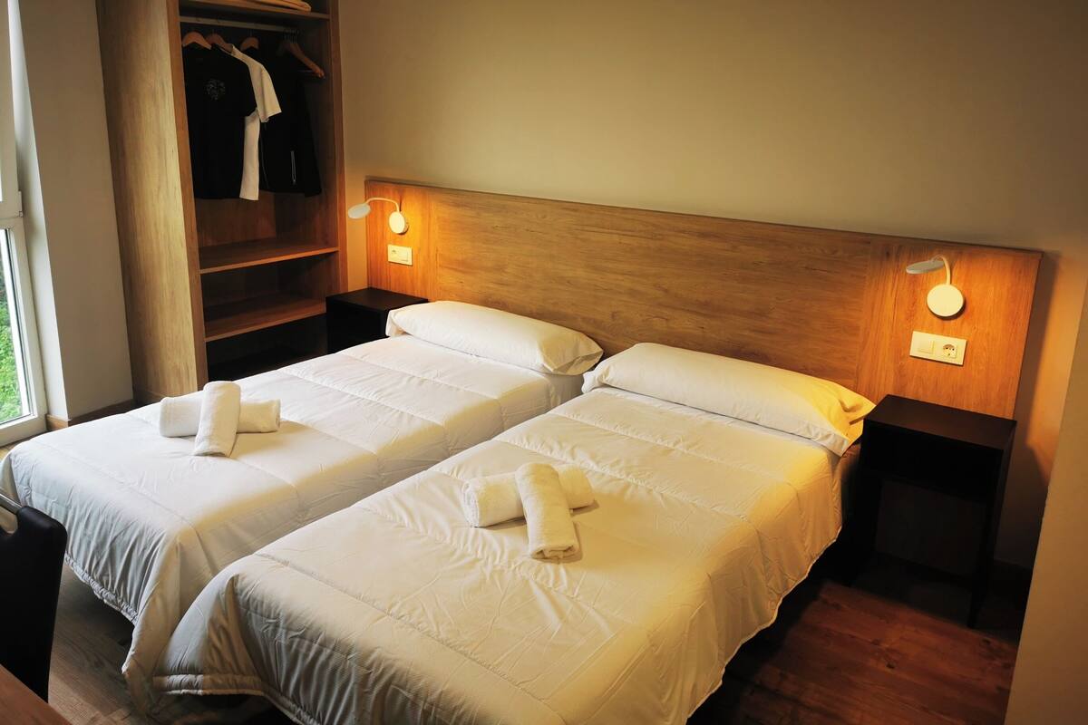 Ein Hotelzimmer mit zwei Betten, einem Holzkopfteil, Nachttischlampen, einem Kleiderschrank und einem Fenster.