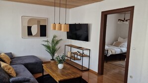 A living room with a sofa, a coffee table, a TV, and a plant. - Holiday Home 'M B Homes Albstadt' with Mountain View, Private Terrace, Wi-Fi & Single Room (Albstadt)
