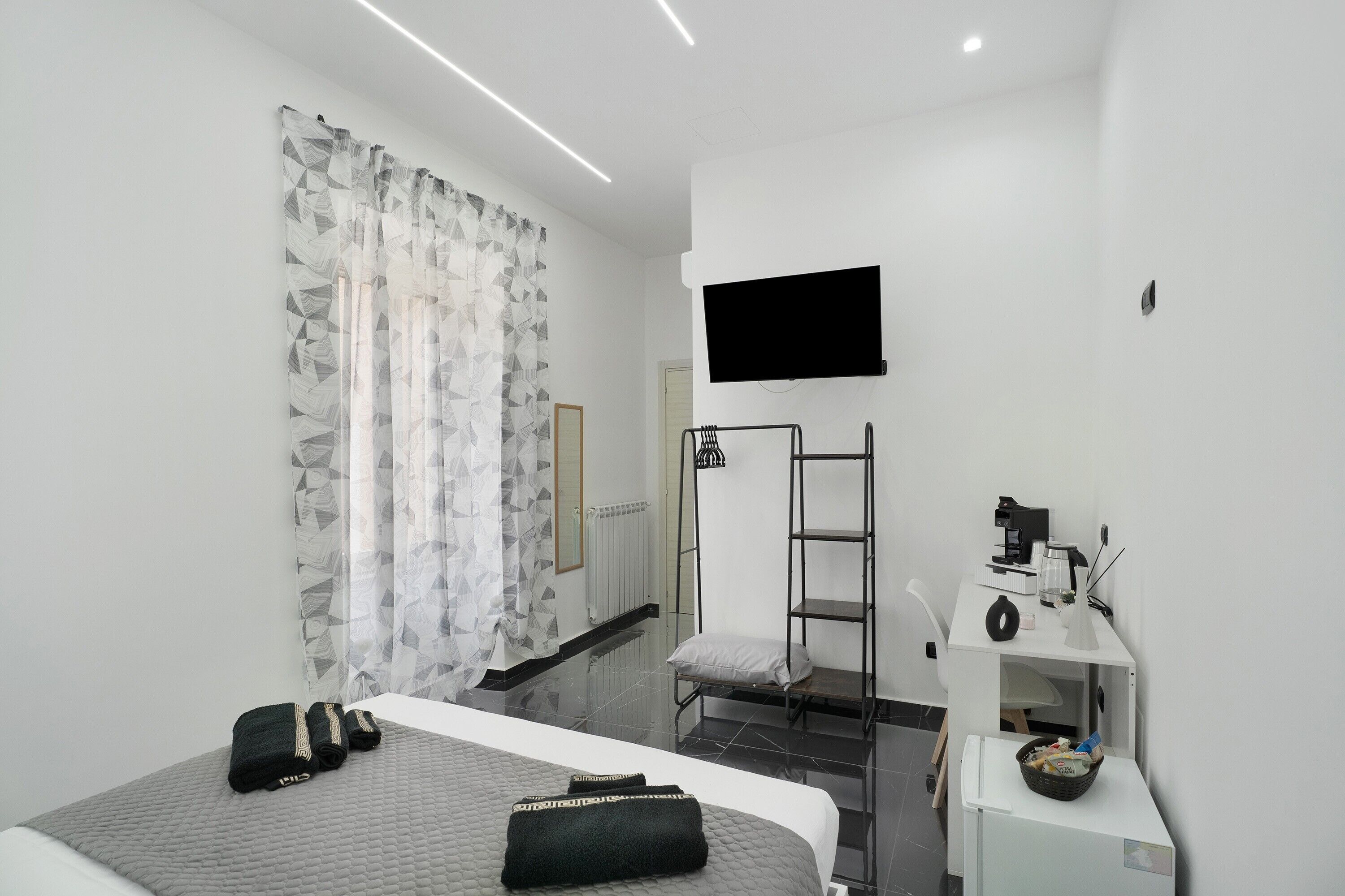 A modern hotel room with a bed, a desk with a computer, a TV mounted on the wall, and a shower area.