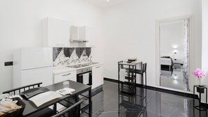 Una cocina moderna con gabinetes blancos, un protector contra salpicaduras de mármol y un comedor con mesa y sillas negras.