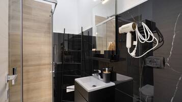 Une salle de bain moderne avec une douche à parois de verre, un lavabo blanc et un sèche-cheveux fixé au mur.