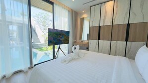 A hotel room with a bed, a painting on a stand, a large window, and a view of a staircase and greenery outside. - Phuvista Villas Naithon - Escape Villas  (Sa Khu)