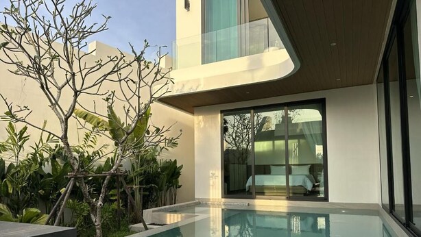 A modern pool area with a clear pool, a wooden deck, and a glass door leading to a room. - Phuvista Villas Naithon - Escape Villas  (Sa Khu)