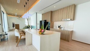 A modern kitchen with a central island, wooden cabinets, and a dining area with white chairs. - Phuvista Villas Naithon - Escape Villas  (Sa Khu)