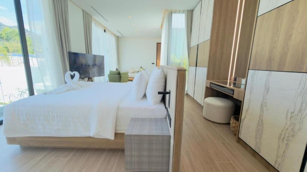 A modern hotel room with a large bed, a flat-screen TV, a small seating area, and a view of the outdoors.