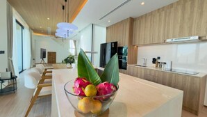 A modern kitchen with a central island, wooden cabinetry, and a dining area with white chairs. - Phuvista Villas Naithon - Escape Villas  (Sa Khu)