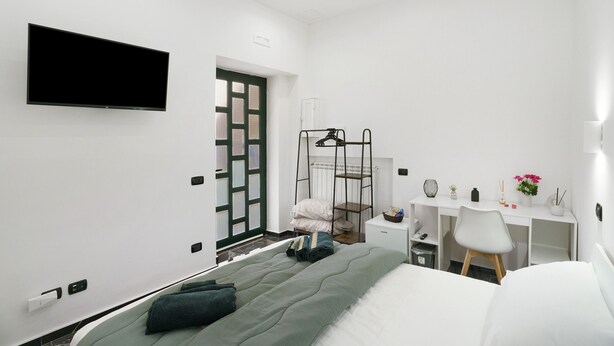A modern bedroom with a bed, a desk, a chair, a TV, and a window.