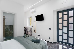 A modern hotel room with a bed, a TV, a desk with a chair, and a door with frosted glass panels. - Black White Room – Queen Standard (Piazza del Galdo-Sant'angelo)