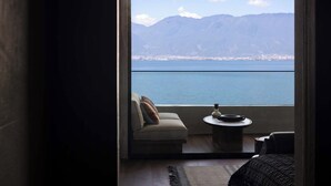 Ένα δωμάτιο με έναν καναπέ και ένα μικρό τραπέζι, θέα σε μια λίμνη ή θάλασσα και σε βουνά, καθώς και μια πόρτα που οδηγεί σε μπαλκόνι.